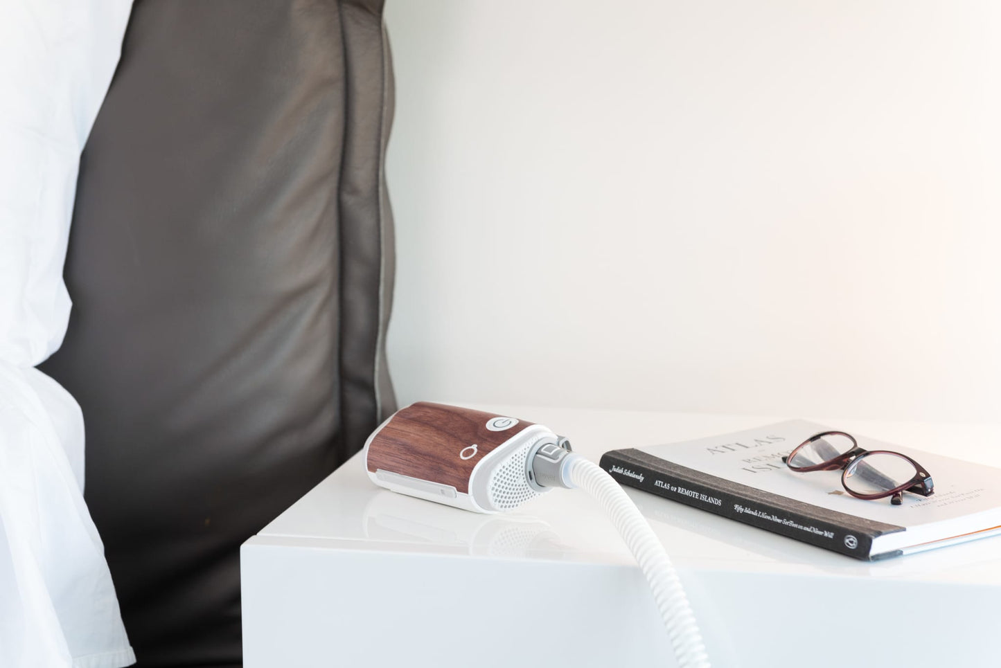 Dark wood Snugell skin on AirMini Travel CPAP Machine with a book and glasses, emphasizing stylish and discreet CPAP machine protection.