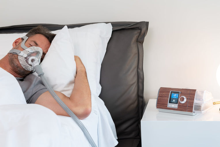 Man sleeping with a CPAP mask next to an AirSense 10 CPAP machine featuring a Snugell dark wood skin, blending the device with cozy bedroom decor.