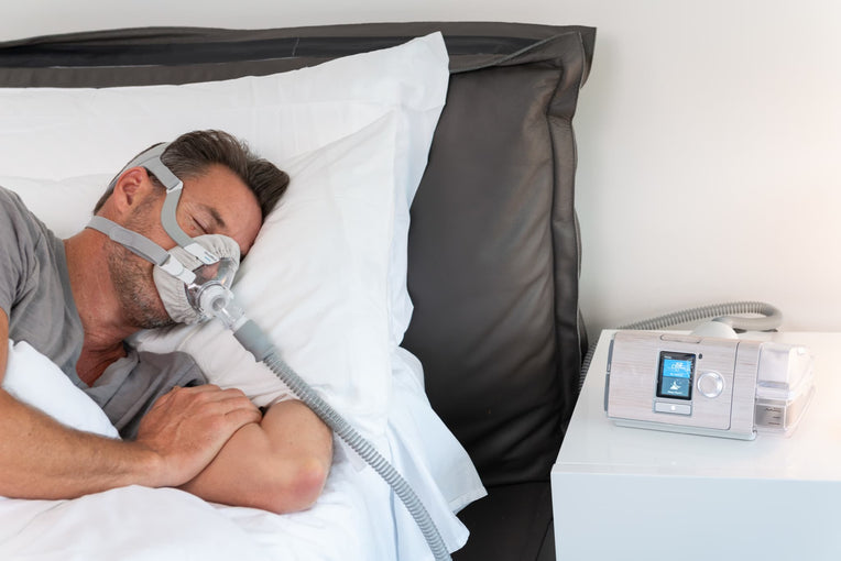 Man sleeping with a CPAP mask next to an AirSense 10 CPAP machine with a Snugell marble skin, adding elegance to his bedroom decor.