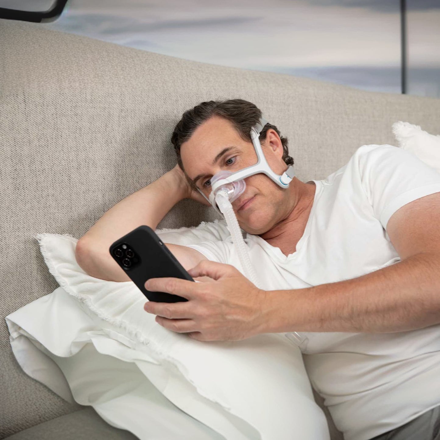 man relaxing in bed scrolling on his phone while wearing  n20