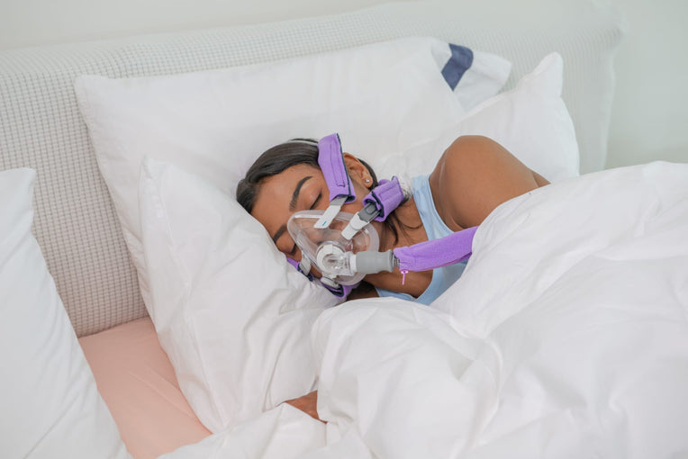 Woman sleeping on her side, wearing a CPAP mask with Snugell CPAP strap covers in purple for added comfort.