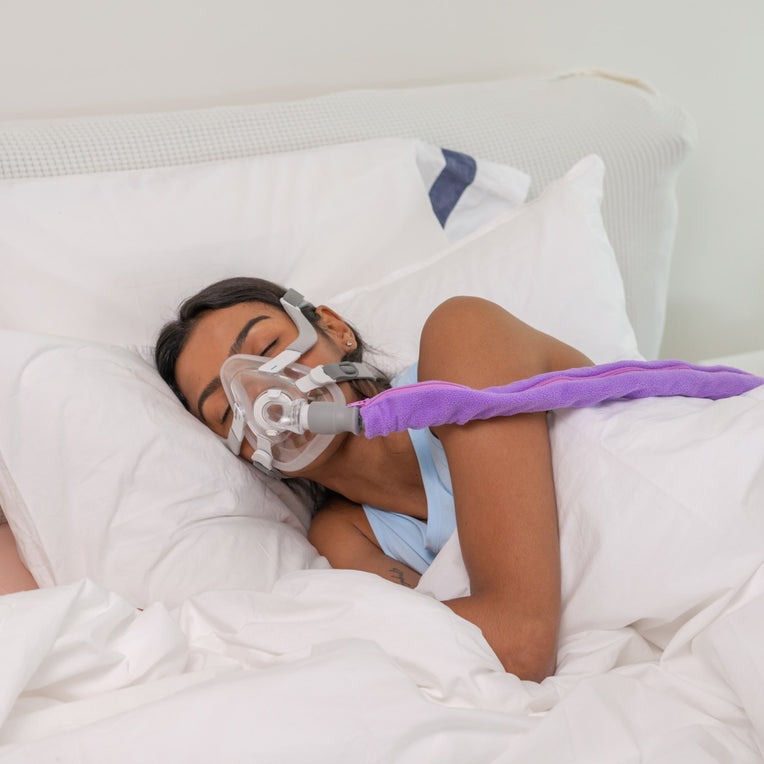 Woman sleeping with a CPAP mask, using a Snugell purple CPAP hose cover to reduce condensation and add comfort.